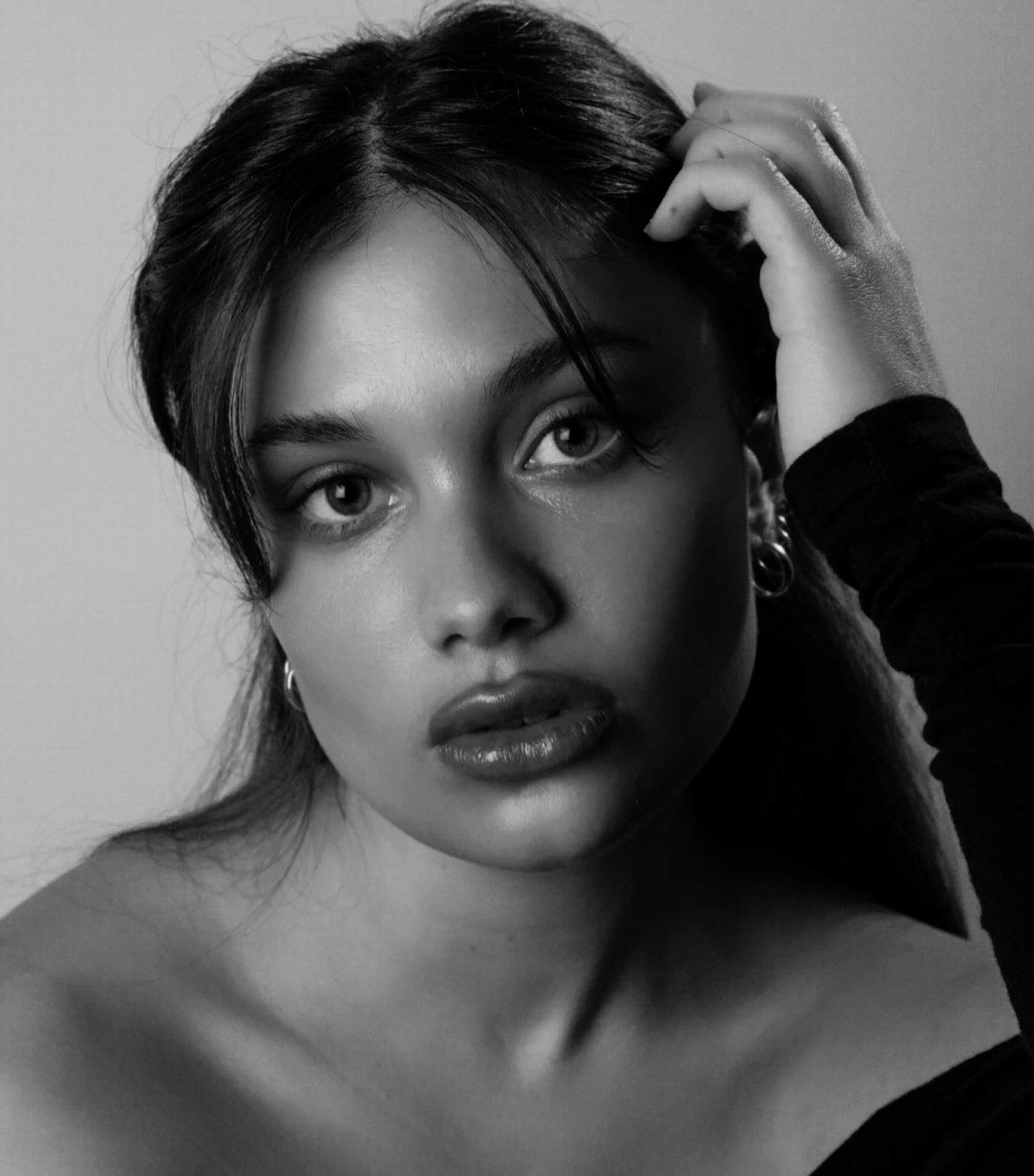 Black and white close portrait of Merivelle, one hand in her hair, looking to camera.