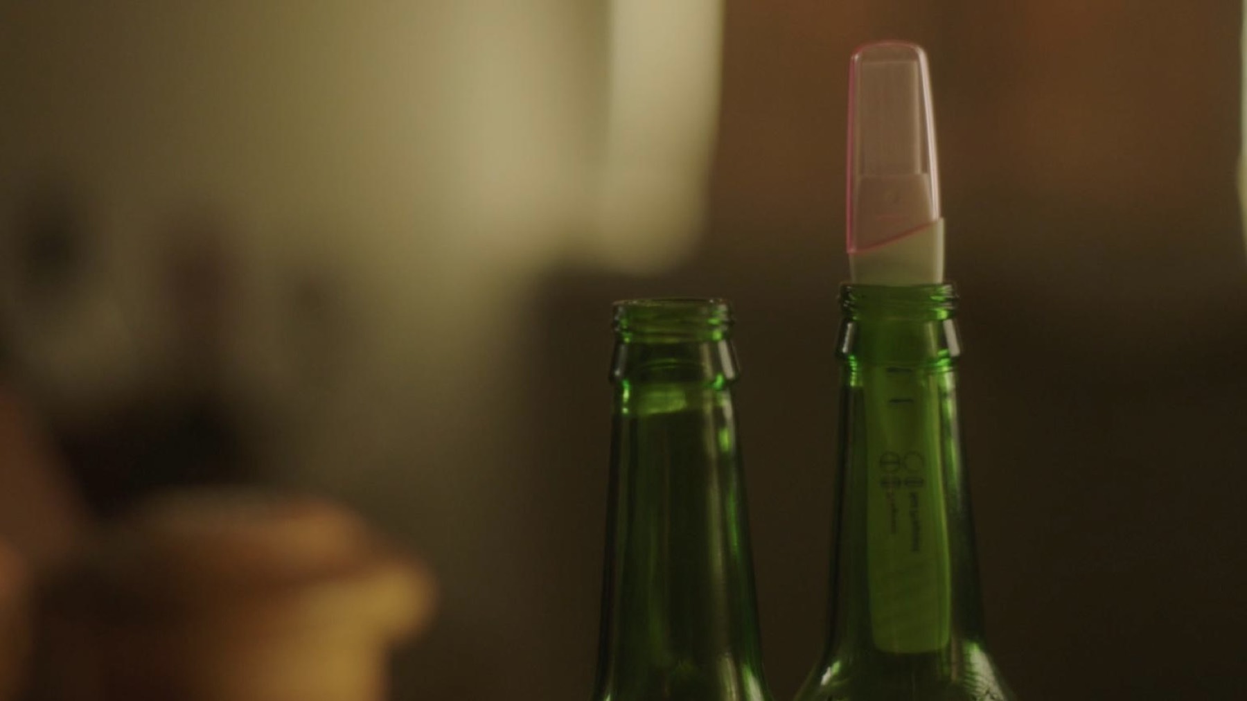 Still from Opa, directed by Merivelle: a pregnancy test resting in the neck of a green beer bottle.
